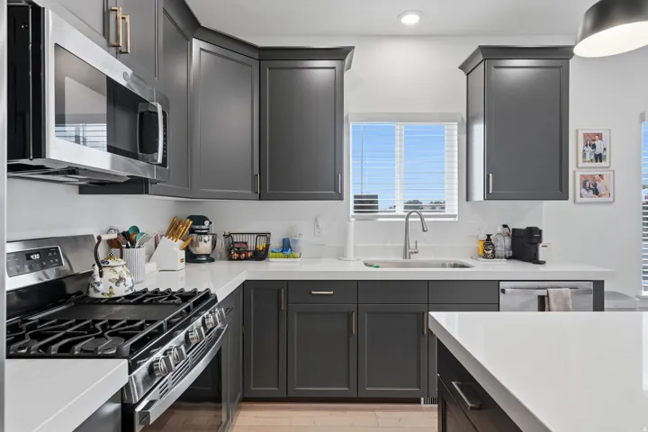 Kitchen featuring dark gray cabinetry, white countertops, stainless steel appliances, and a stainless steel sink with a gooseneck faucet