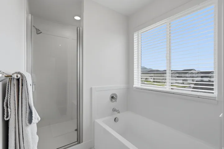 Bathtub with chrome fixtures, an adjacent shower with a glass enclosure, and a large window with horizontal blinds