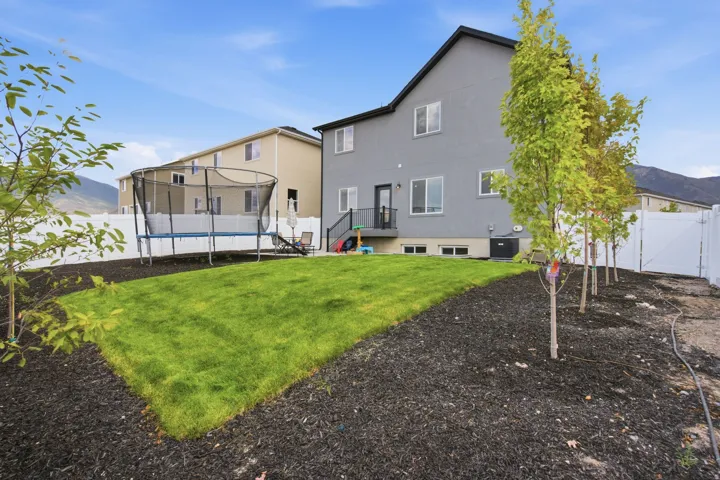 Expansive backyard featuring a manicured lawn, established trees, dark ground cover, and a full privacy fence