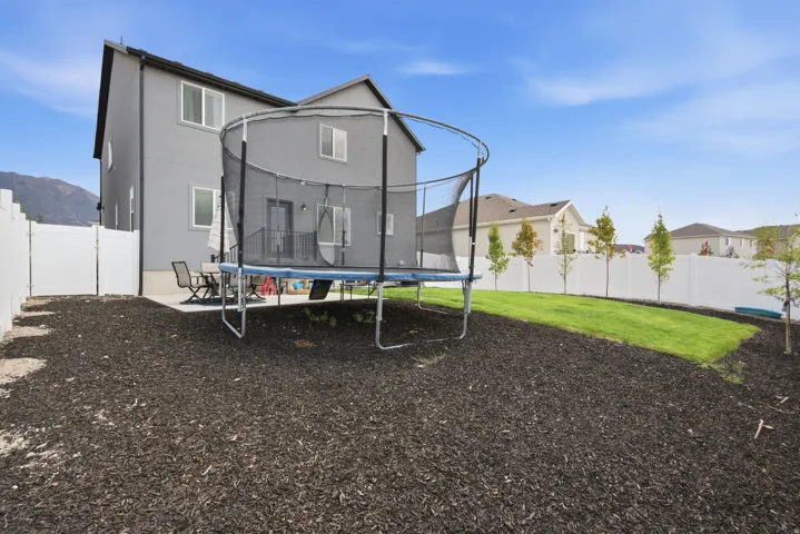 Expansive backyard featuring a manicured lawn, mulched areas, a concrete patio, and a privacy fence