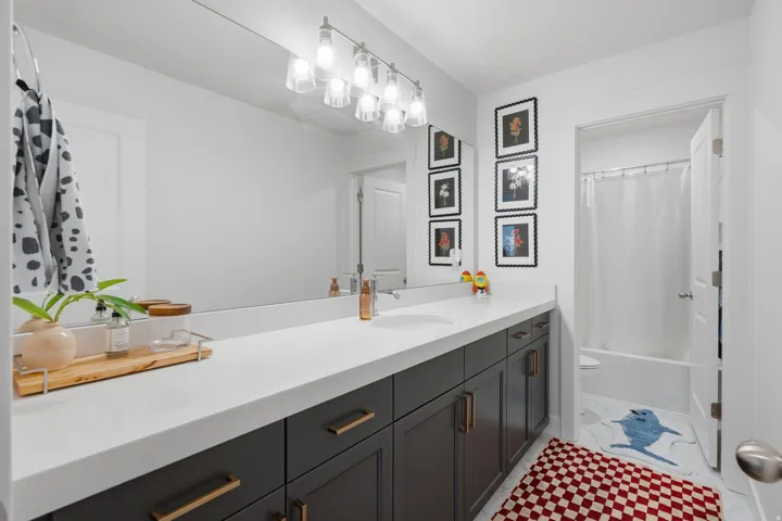 White countertop vanity with under-mount sink, dark wood-finish cabinetry, and brushed brass hardware