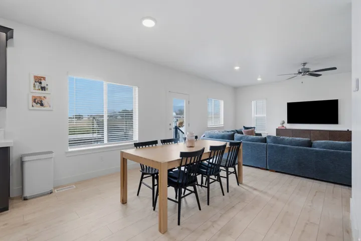 Bright open-concept living area with light wood-finish flooring, recessed lighting, and a ceiling fan
