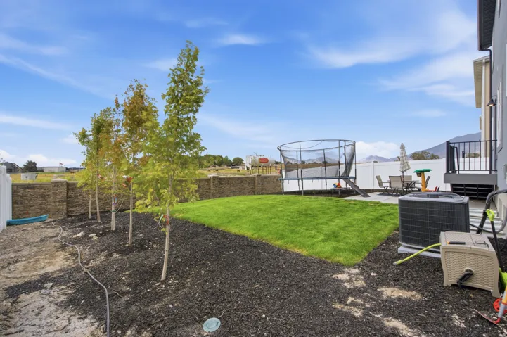 Expansive backyard featuring a newly seeded lawn, mature landscaping with multiple trees, black mulch beds, and a trampoline