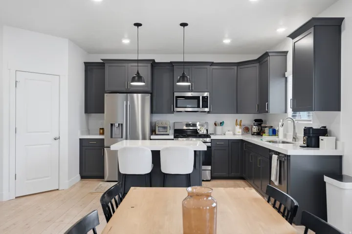 Kitchen featuring dark cabinetry, stainless steel appliances, a center island with pendant lighting, light wood-finish flooring, and white countertops