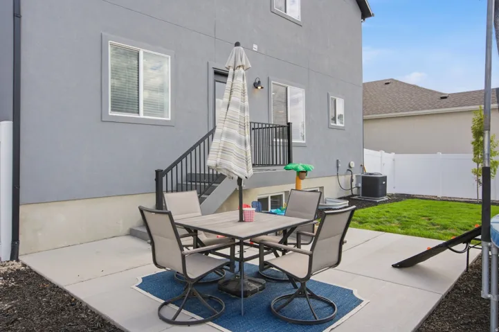 Exterior patio space featuring a concrete pad, dark gray stucco siding, black metal handrails, and a manicured lawn