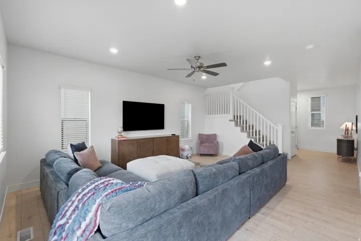 Recessed lighting, ceiling fan, wood-finish flooring, staircase with white railing, and multiple windows with blinds