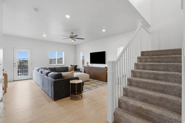Recessed lighting, wood-finish flooring, white painted walls, ceiling fan, and carpeted stairs with white balusters
