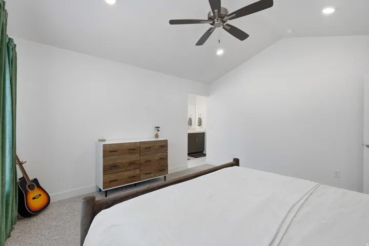 Vaulted ceiling, recessed lighting, ceiling fan, carpet flooring, and a door leading to an adjoining area with a vanity
