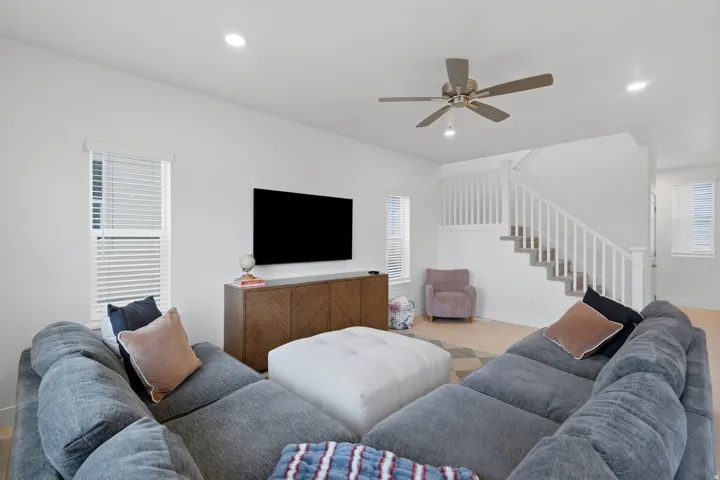 Recessed lighting, ceiling fan, wood-finish flooring, white walls, and a staircase with white balusters