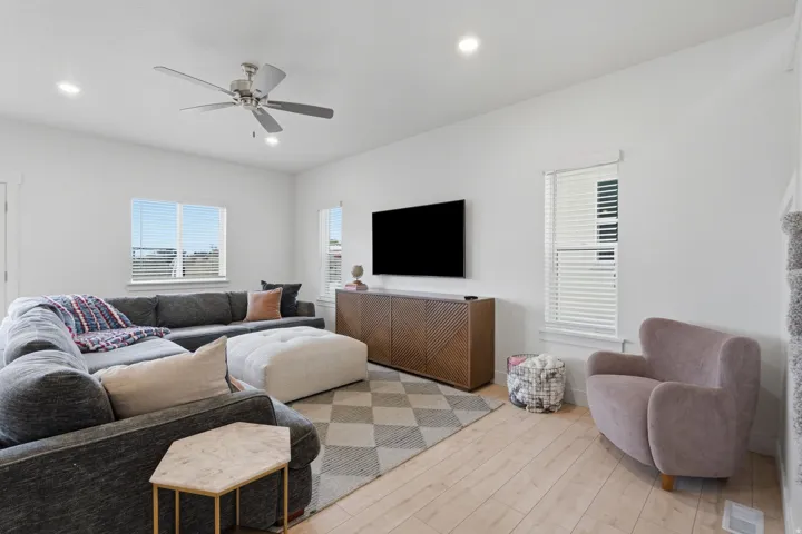 Recessed lighting, ceiling fan, multiple windows with blinds, wood-finish flooring, and a built-in media console