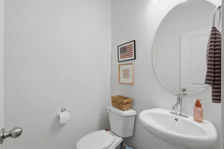 Pedestal sink with chrome faucet, circular mirror, and white toilet