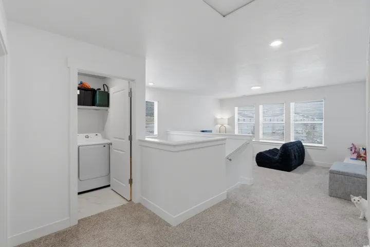 Carpeted landing featuring a laundry closet with shelving, recessed lighting, and multiple windows with blinds