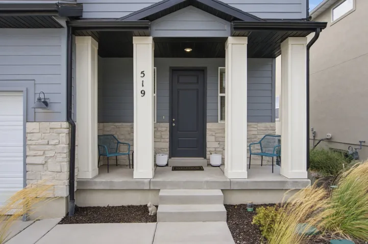 Covered entry porch with white columns, horizontal siding, stone veneer accents, and a dark-paneled door