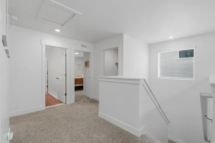 Recessed ceiling lighting, white walls, light-colored carpeting, a window with horizontal blinds, and white trim throughout