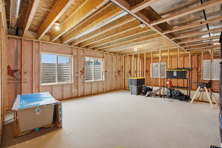 Unfinished basement with exposed wood framing, concrete flooring, and multiple egress windows
