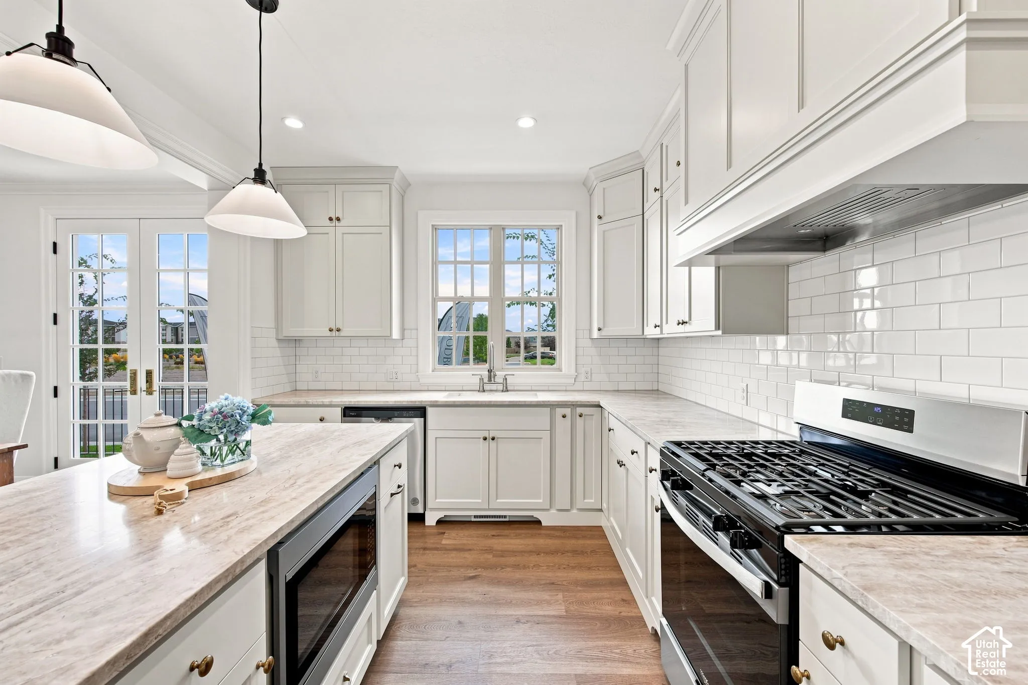 Model Home - Kitchen featuring white cabinetry, subway tile backsplash, wood-finish flooring, a kitchen island with built-in microwave, and stainless steel appliances