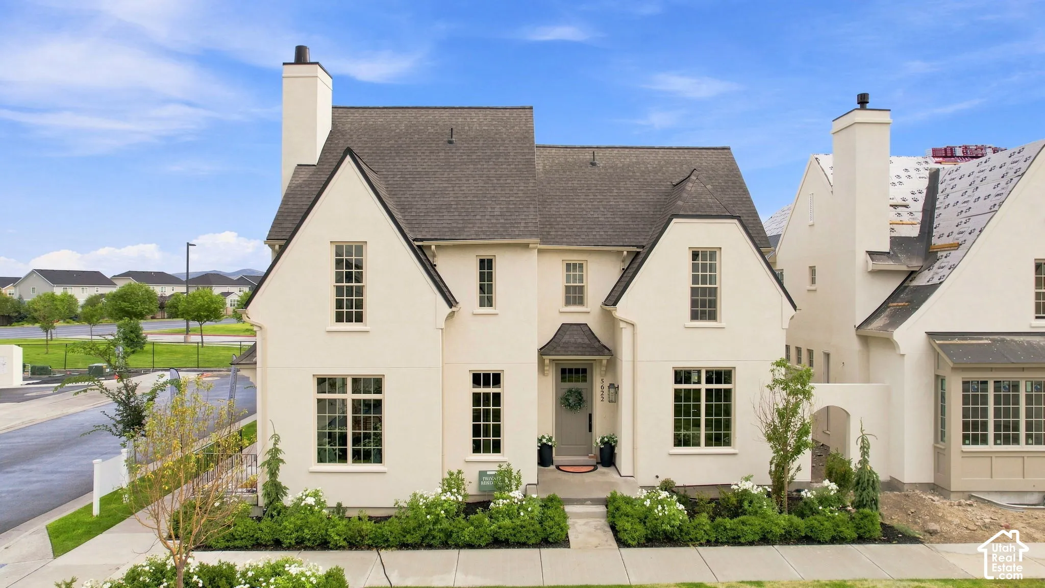 Model Home - Cream-colored stucco exterior with a dark shingle roof, multiple gables, and prominent chimneys