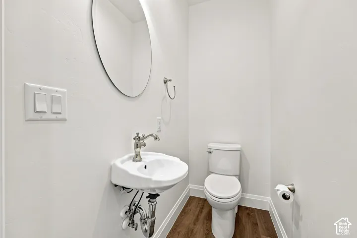 Model Home - Pedestal sink with polished chrome faucet, oval mirror, white toilet, and wood-finish flooring