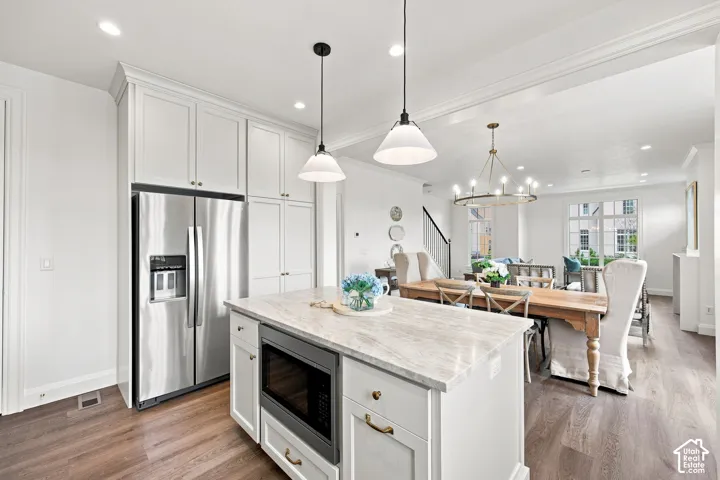 Model Home - Kitchen with white shaker cabinetry, stainless steel refrigerator, and a center island with a built-in microwave and stone countertop