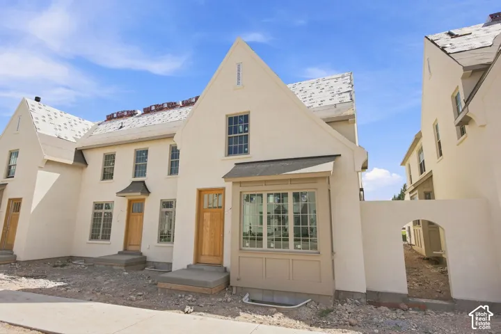 Stucco exterior with gabled rooflines, prominent bay window, light wood-finish entry doors, and arched architectural detail