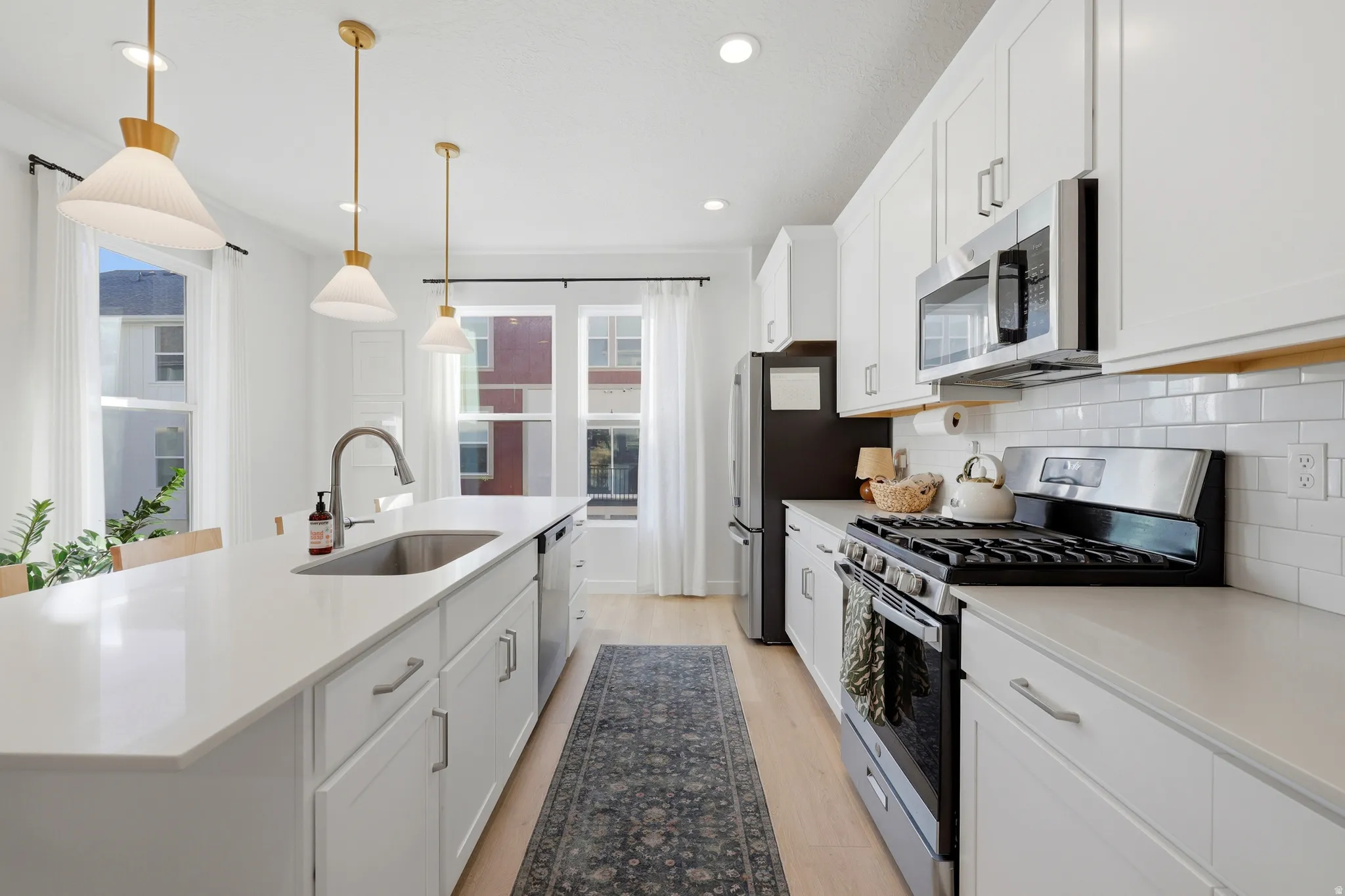 Kitchen featuring white cabinetry, light-toned wood-finish flooring, stainless steel appliances, a center island with a sink, and pendant lighting