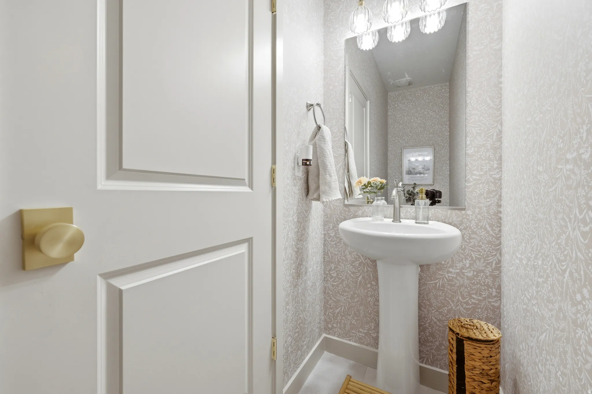 Pedestal sink with polished chrome faucet, decorative wall covering, rectangular mirror, and three-light vanity fixture