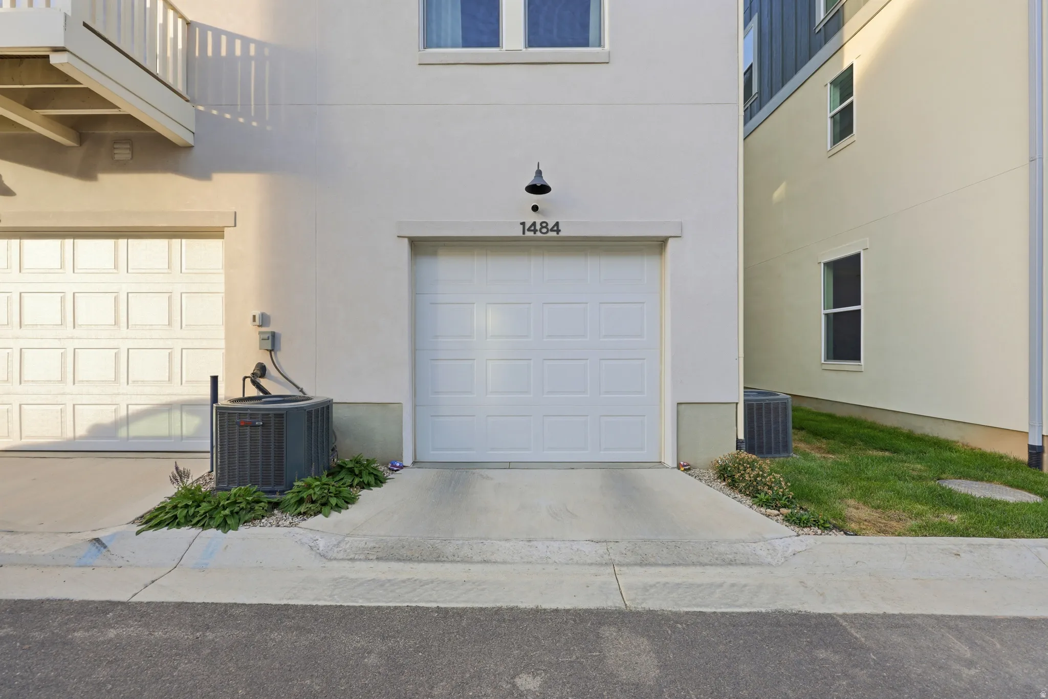 White paneled garage door with black hardware and address plaque, concrete driveway, and manicured landscaping with fresh lawn and shrub plantings flanking the entry