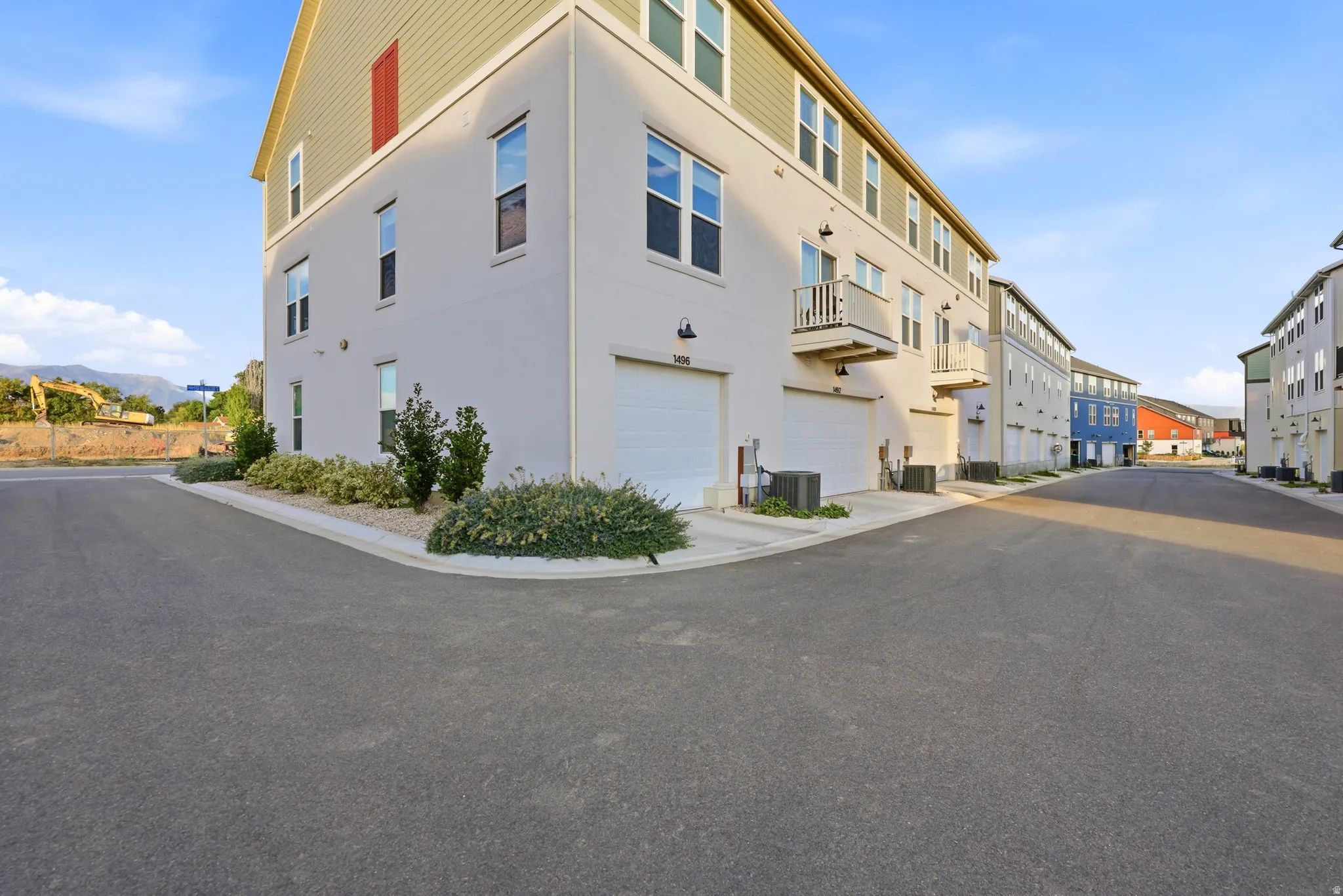 Modern corner-unit townhome featuring a crisp white exterior with horizontal siding, multiple windows providing natural light, and a rounded corner entry with landscaped foundation plantings