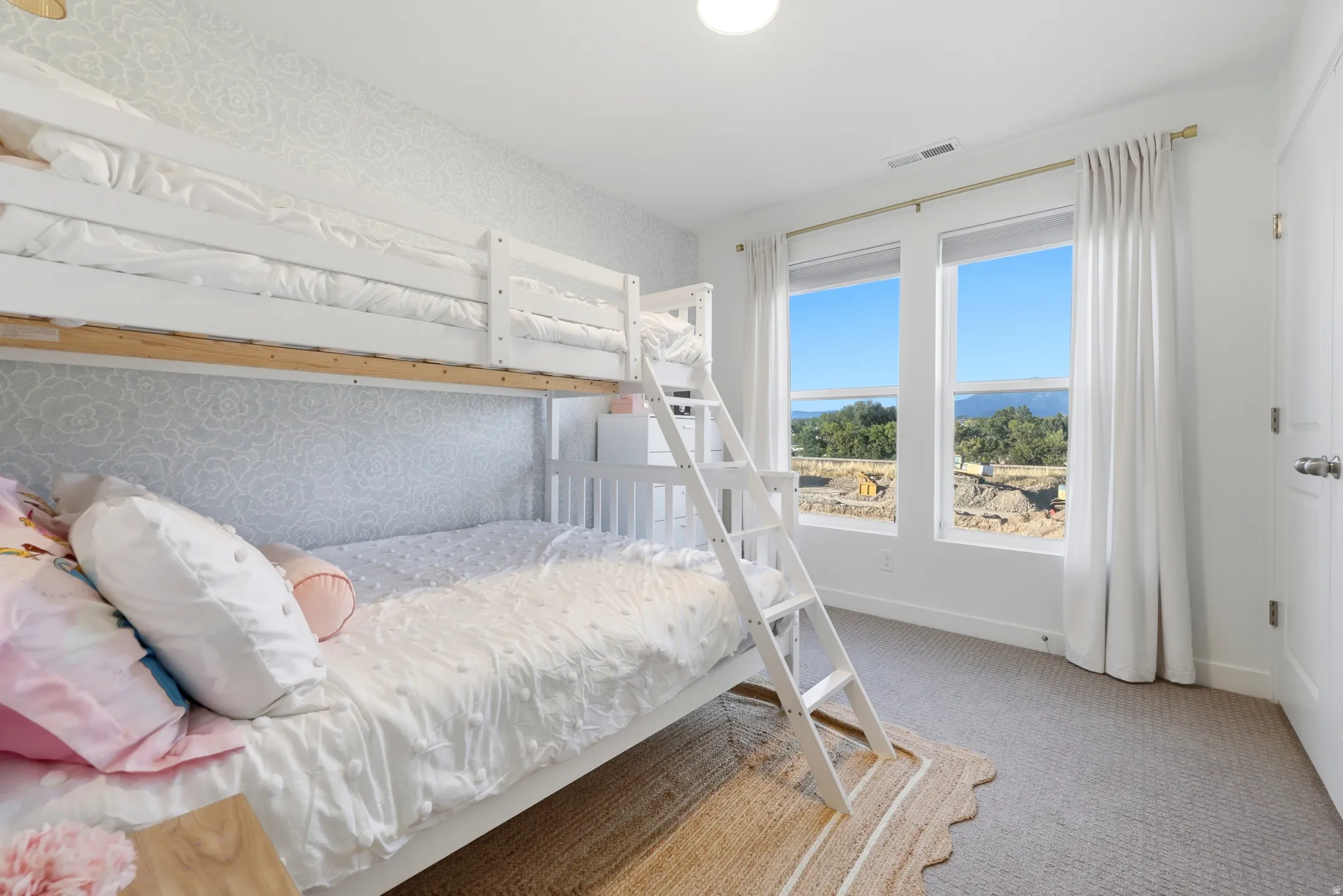 Textured wall covering with a floral pattern, dual windows with white trim, and light-colored carpeting
