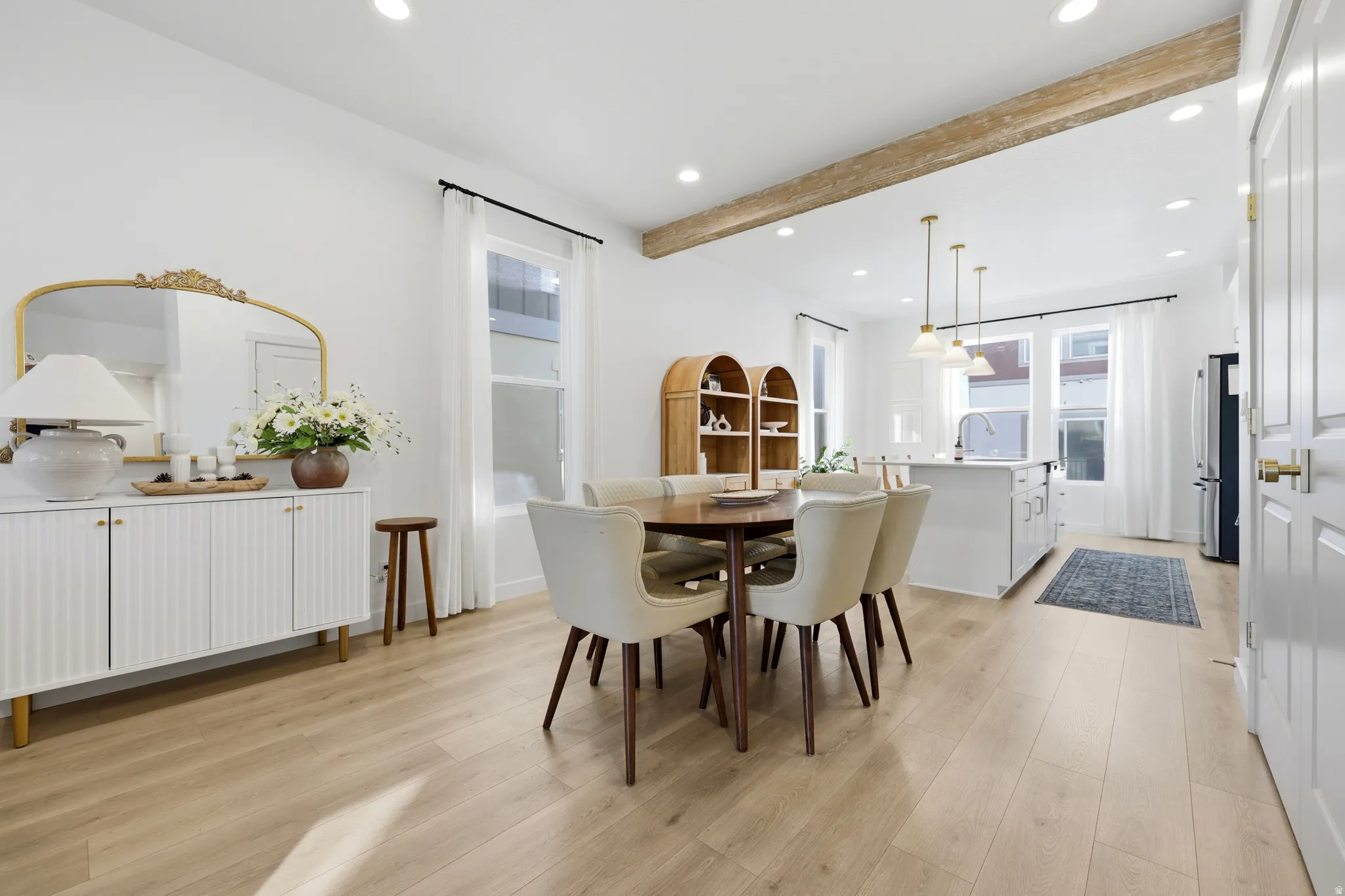 Open-concept dining and kitchen area showcasing wood-finish flooring, recessed ceiling lighting, and exposed wooden beam detailing