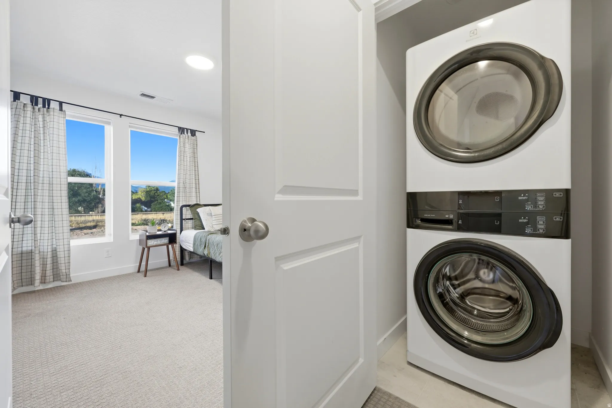 Integrated laundry closet with stacked appliances, featuring white doors and light-colored flooring
