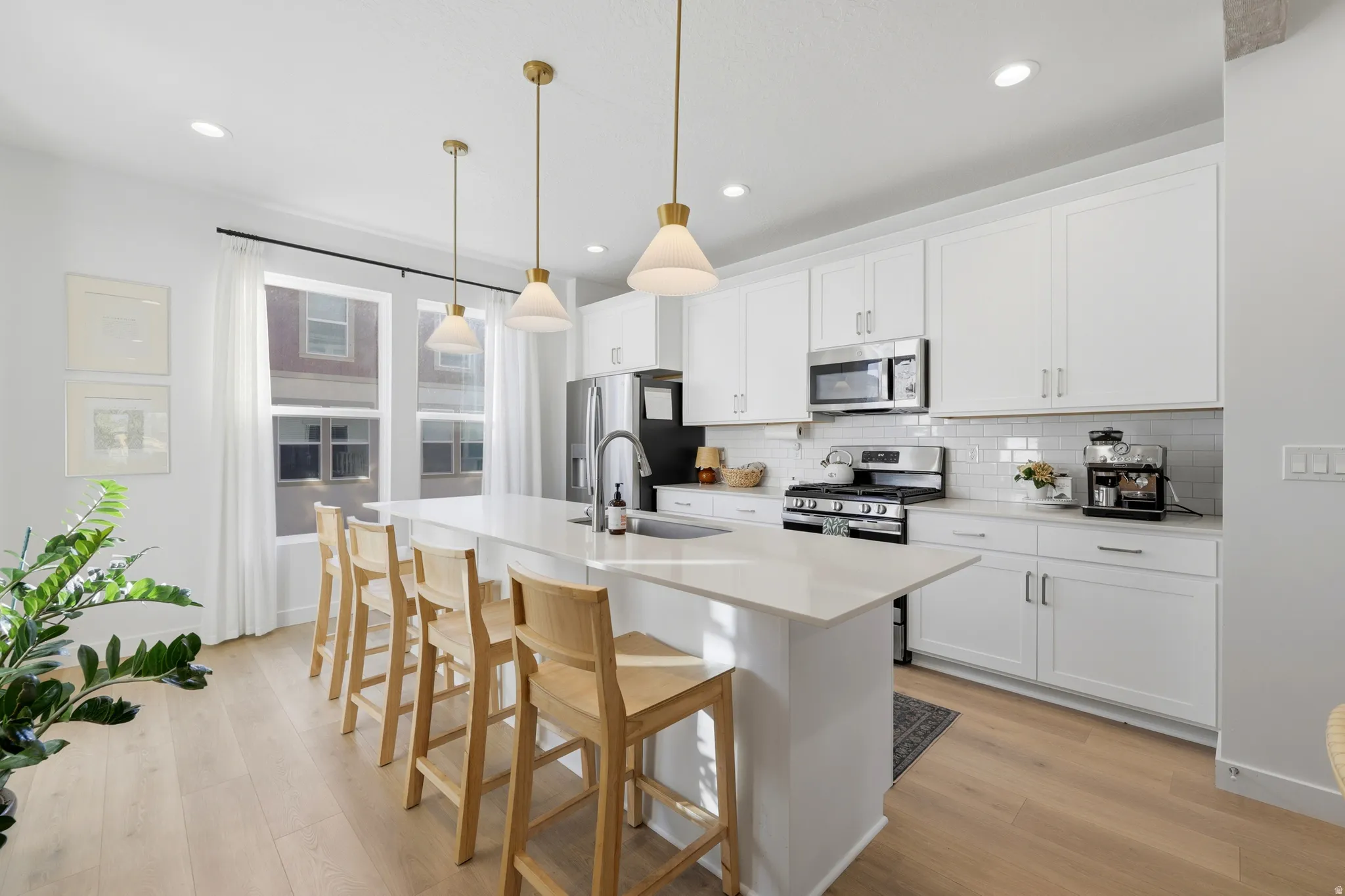 Modern kitchen featuring an expansive island with seating, white shaker cabinetry, stainless steel appliances, and wood-finish flooring