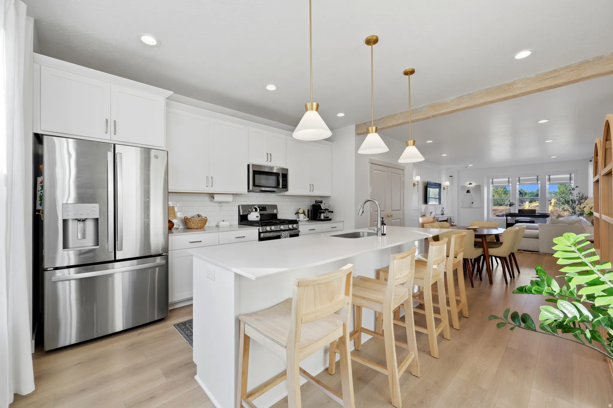 Chef's kitchen featuring stainless steel French-door refrigerator, white cabinetry with hardware accents, quartz waterfall island countertop, pendant lighting with brass fixtures, and seamless integration into the open-concept living area with wood-finish