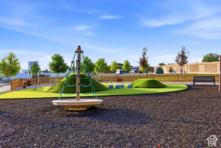 Modern recreational park featuring a multi-level playground structure with integrated slide and climbing elements, surrounded by manicured lawn areas and dark mulch surfacing