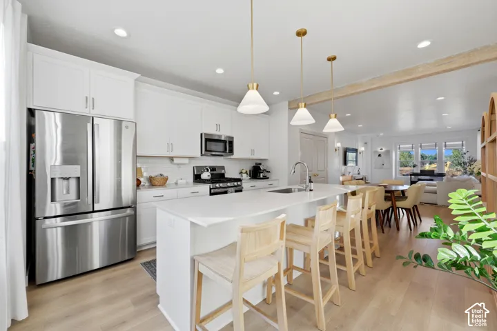 Chef's kitchen featuring stainless steel French-door refrigerator, white cabinetry with hardware accents, quartz waterfall island countertop, pendant lighting with brass fixtures, and seamless integration into the open-concept living area with wood-finish
