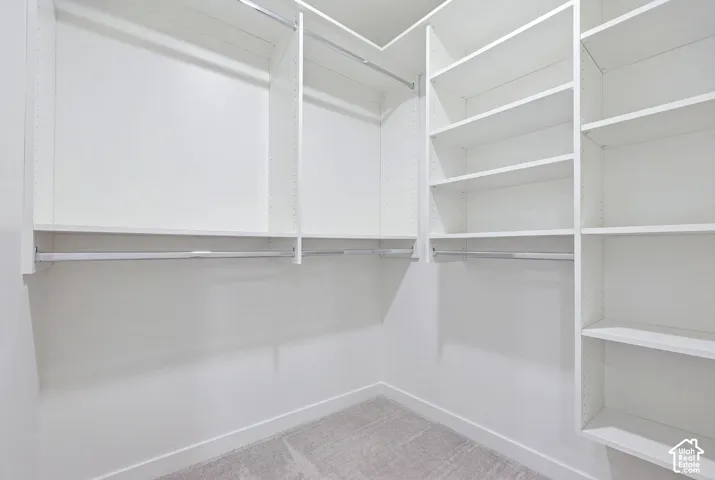 Spacious walk-in closet featuring white custom shelving with multiple storage levels, polished metal rods for hanging space, and soft-finish flooring throughout