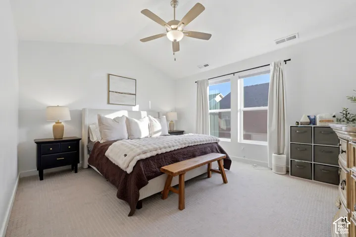 Spacious primary bedroom featuring neutral carpet flooring, ceiling fan with integrated lighting, dual nightstands with table lamps, and expansive glass sliding doors opening to natural light