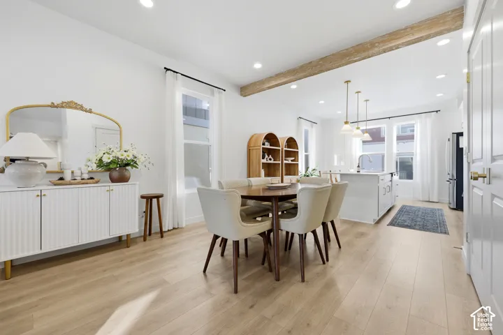 Open-concept dining and kitchen area showcasing wood-finish flooring, recessed ceiling lighting, and exposed wooden beam detailing