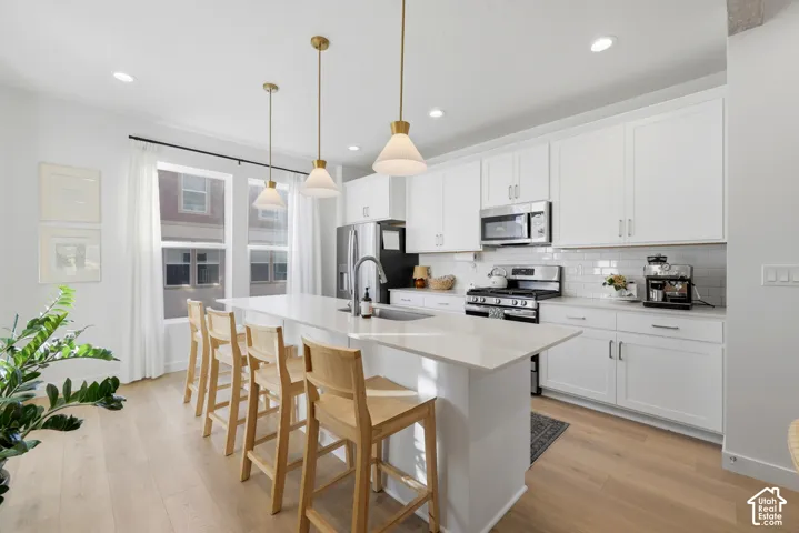 Modern kitchen featuring an expansive island with seating, white shaker cabinetry, stainless steel appliances, and wood-finish flooring