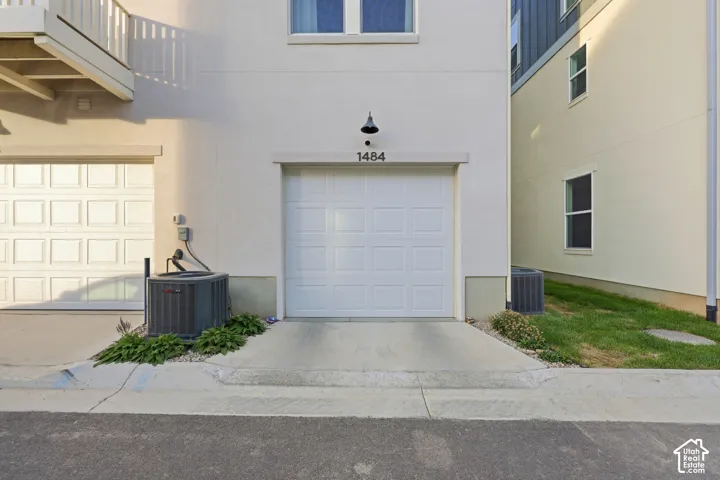White paneled garage door with black hardware and address plaque, concrete driveway, and manicured landscaping with fresh lawn and shrub plantings flanking the entry