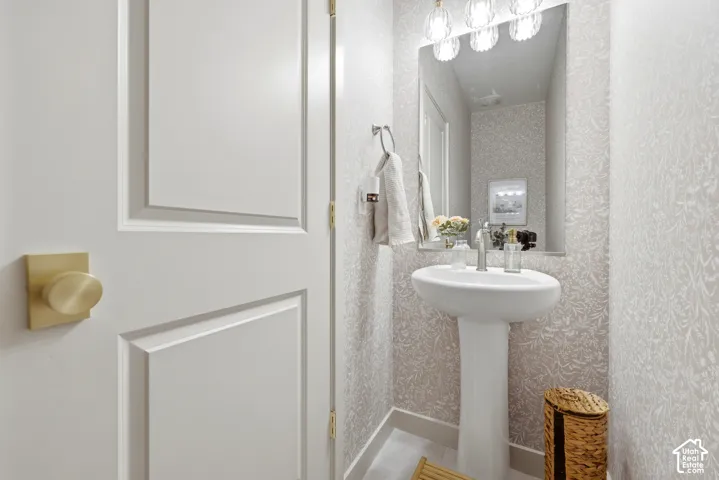 Pedestal sink with polished chrome faucet, decorative wall covering, rectangular mirror, and three-light vanity fixture