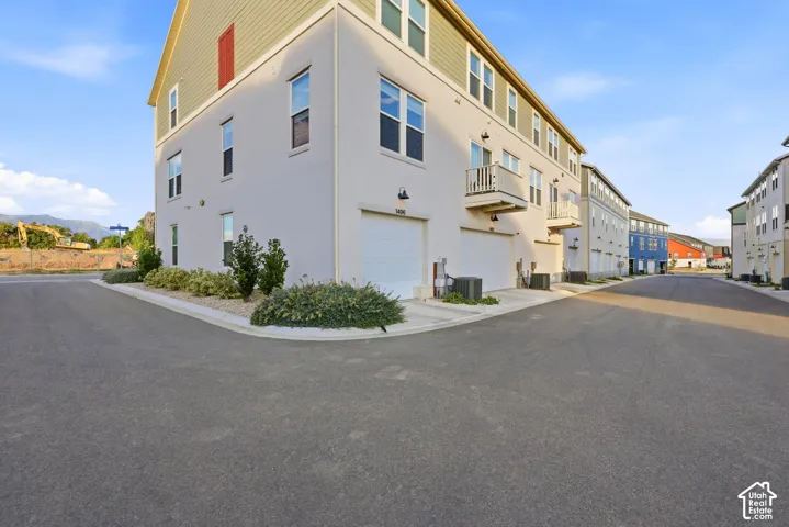 Modern corner-unit townhome featuring a crisp white exterior with horizontal siding, multiple windows providing natural light, and a rounded corner entry with landscaped foundation plantings