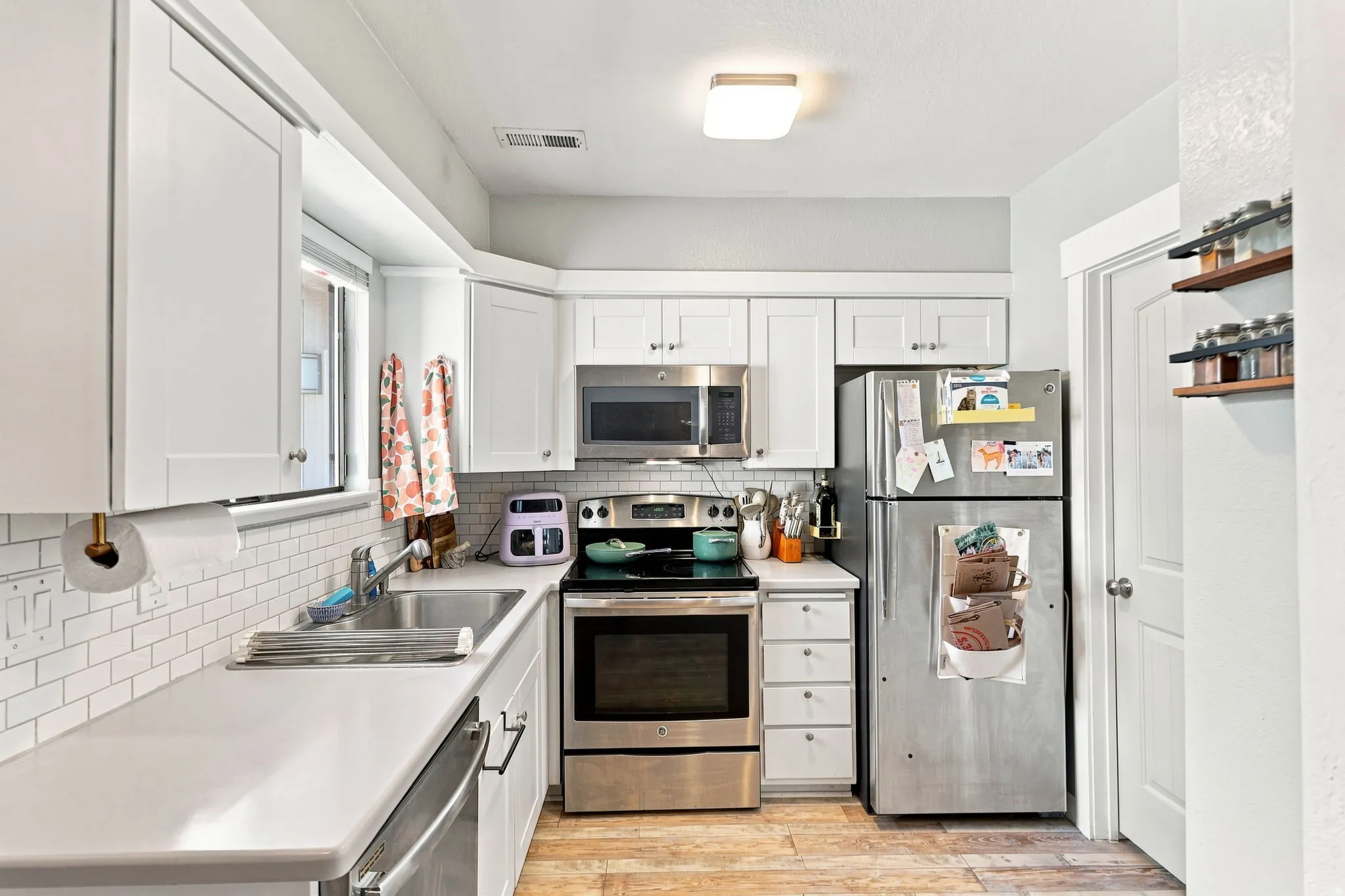 White cabinetry, stainless steel appliances, subway tile backsplash, light-toned countertops, and wood-finish flooring