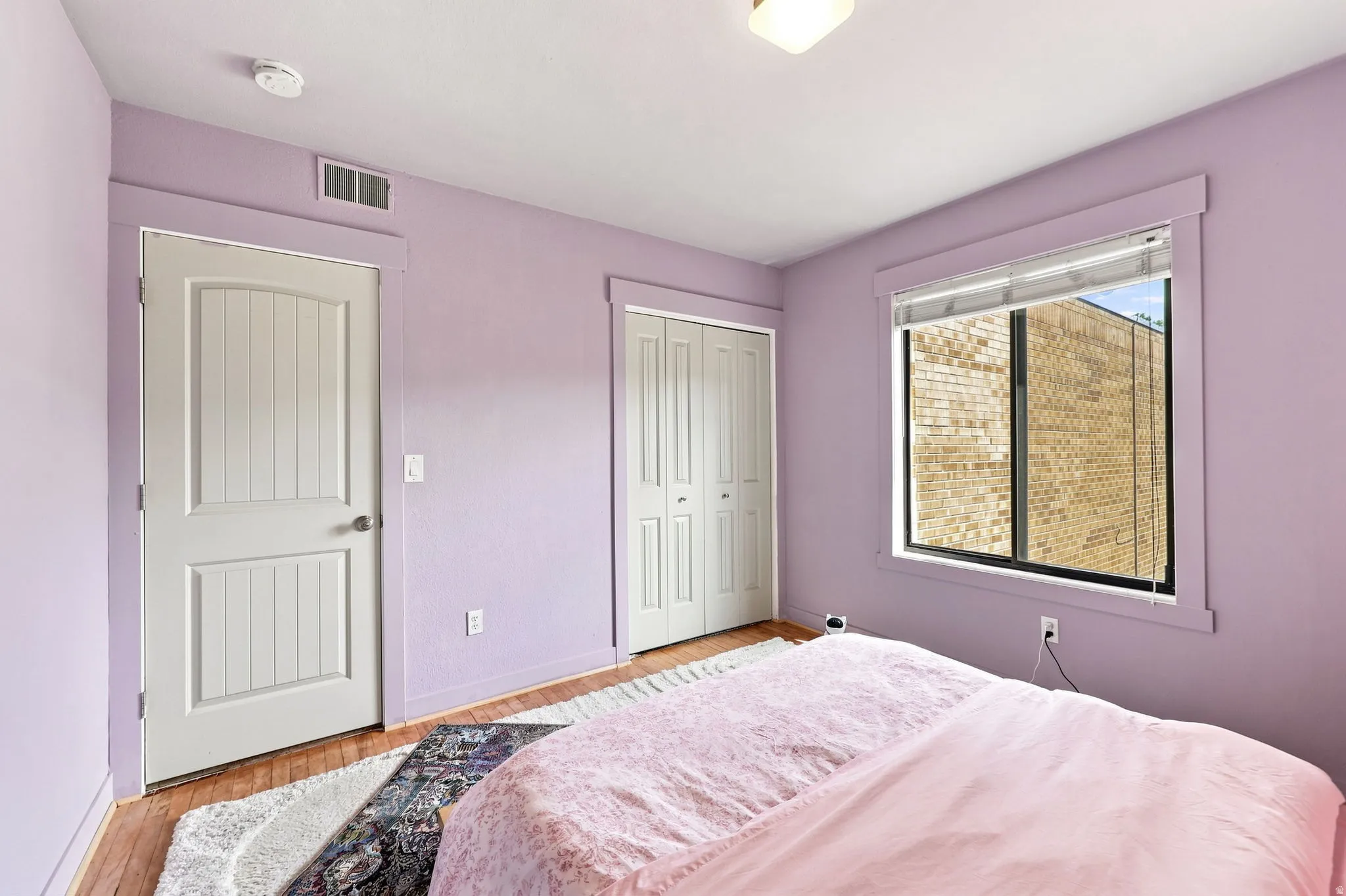 Wood-finish flooring with white trim, built-in closet with bi-fold doors, and a single window with blinds