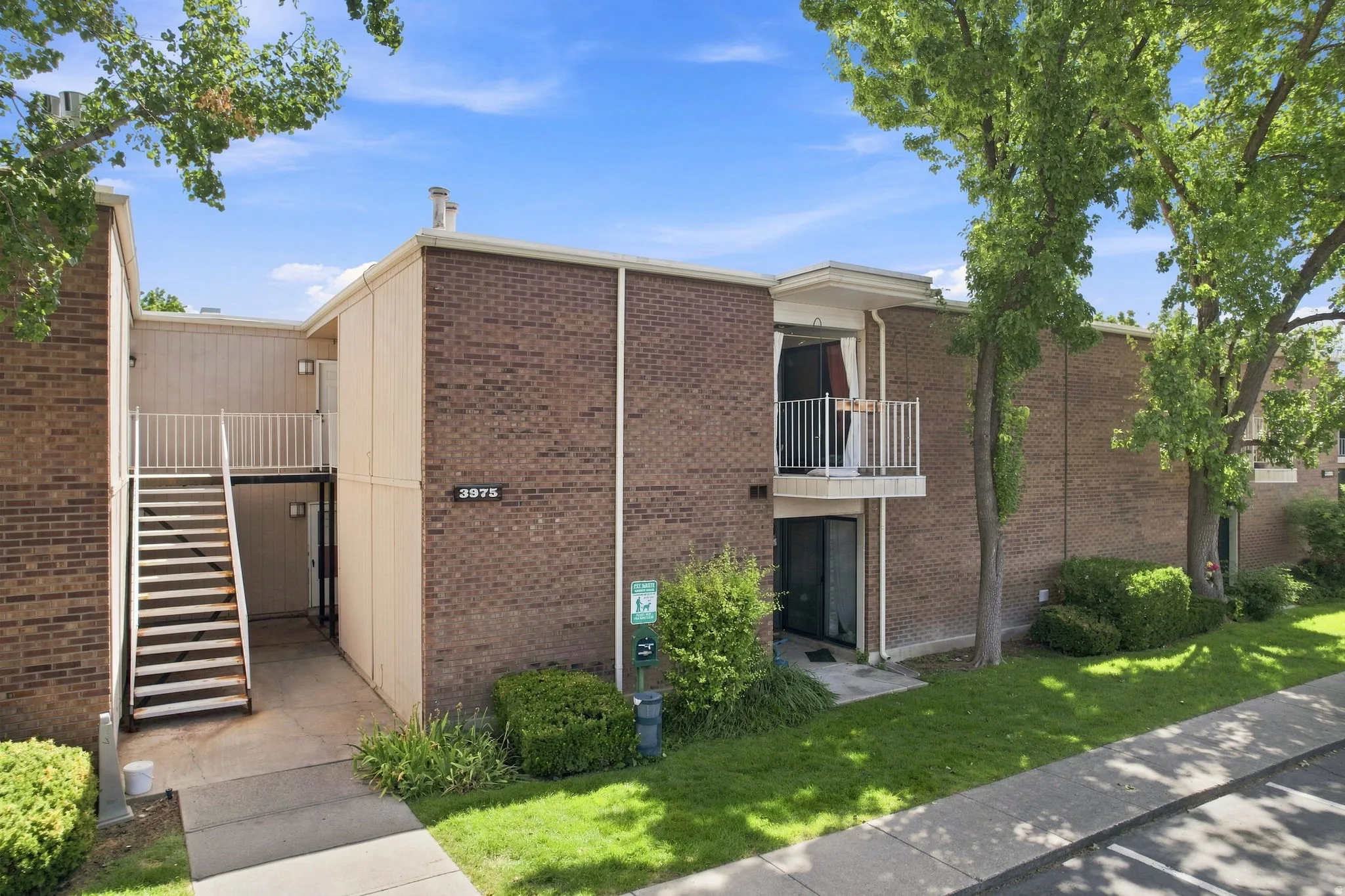 Brick exterior featuring a private balcony with white railing, exterior staircase, and mature landscaping