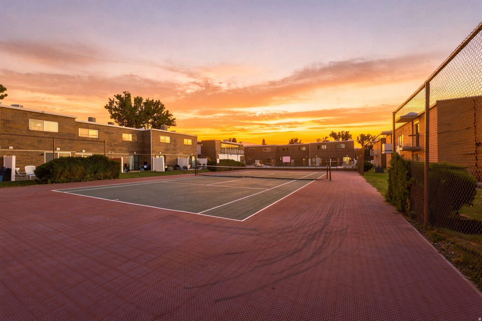 Tennis court with a green and white playing surface, surrounded by a red textured ground