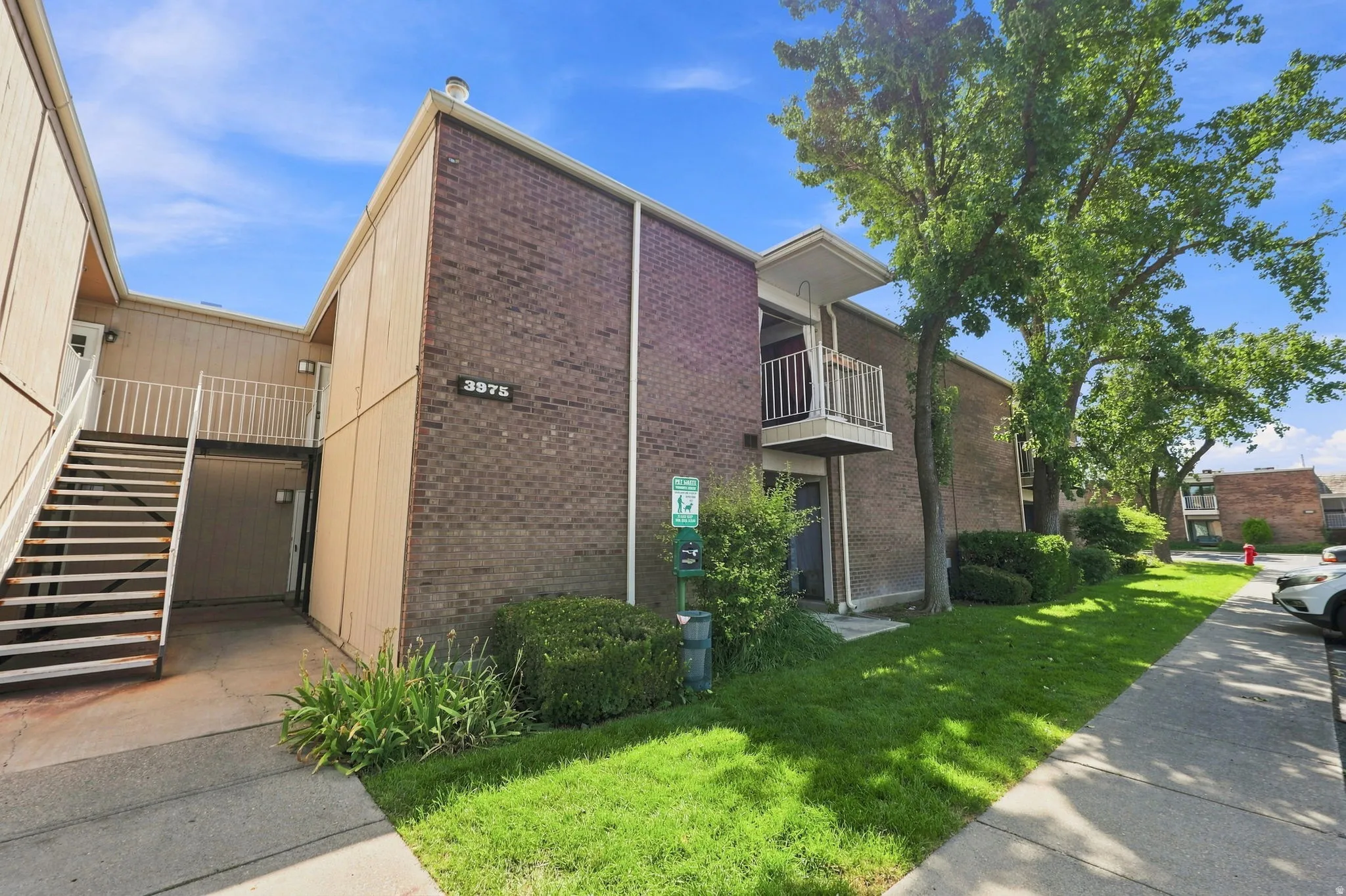 Brick exterior facade, mature landscaping, exterior staircase, concrete walkways, and an upper-level balcony