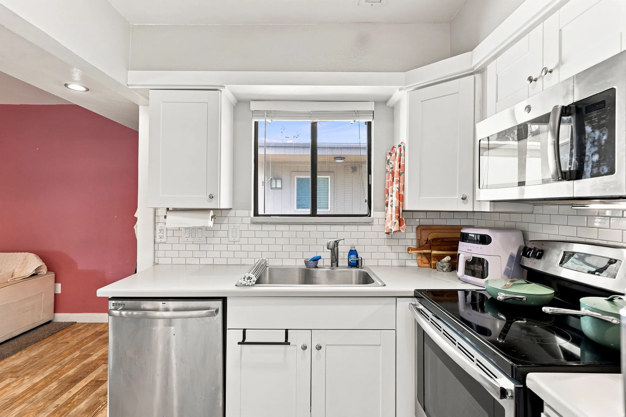 White shaker cabinetry, stainless steel appliances, subway tile backsplash, white countertops, and wood-finish flooring