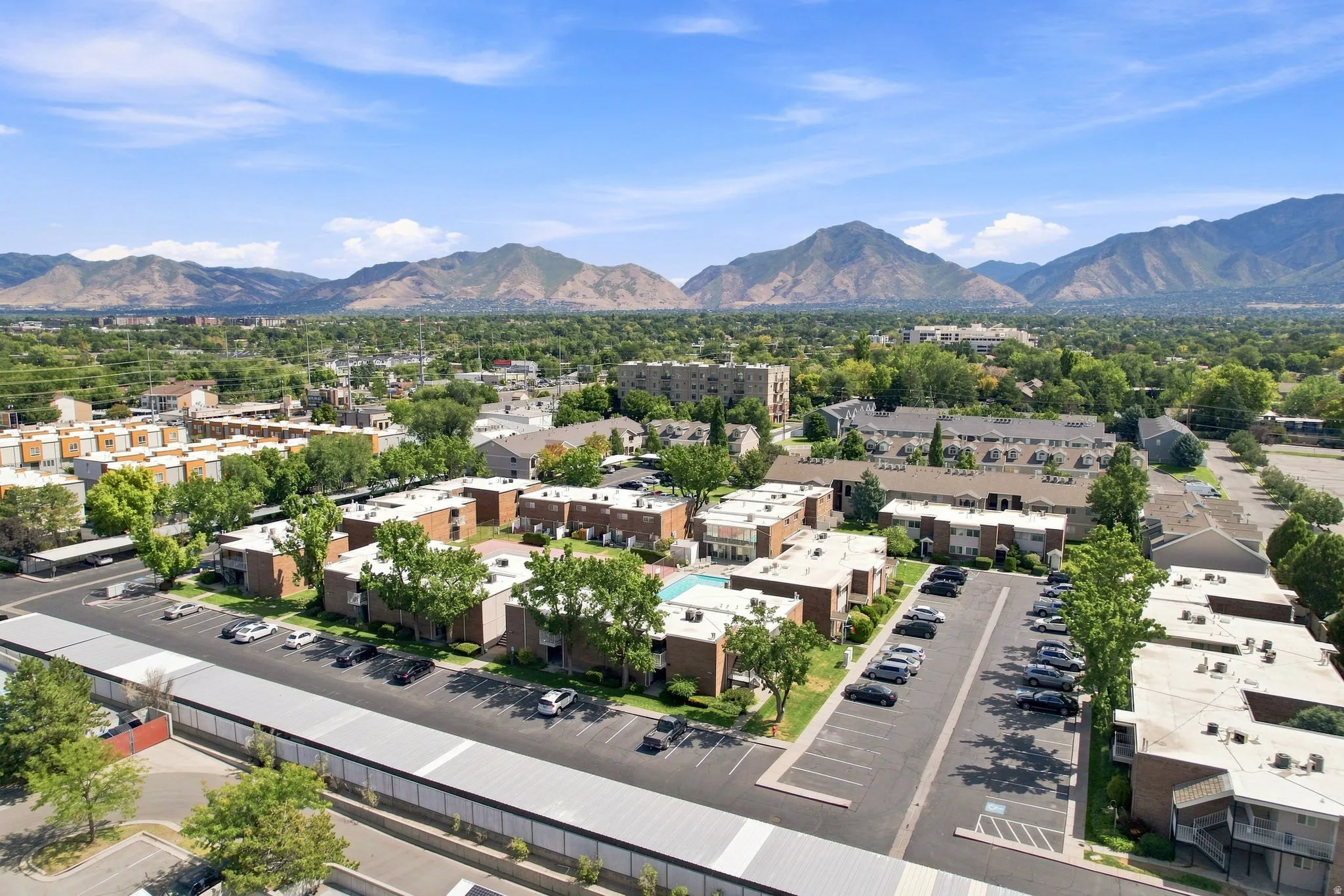 Expansive property with multiple buildings, surface parking, mature trees, and a central swimming pool, all set against a mountainous backdrop