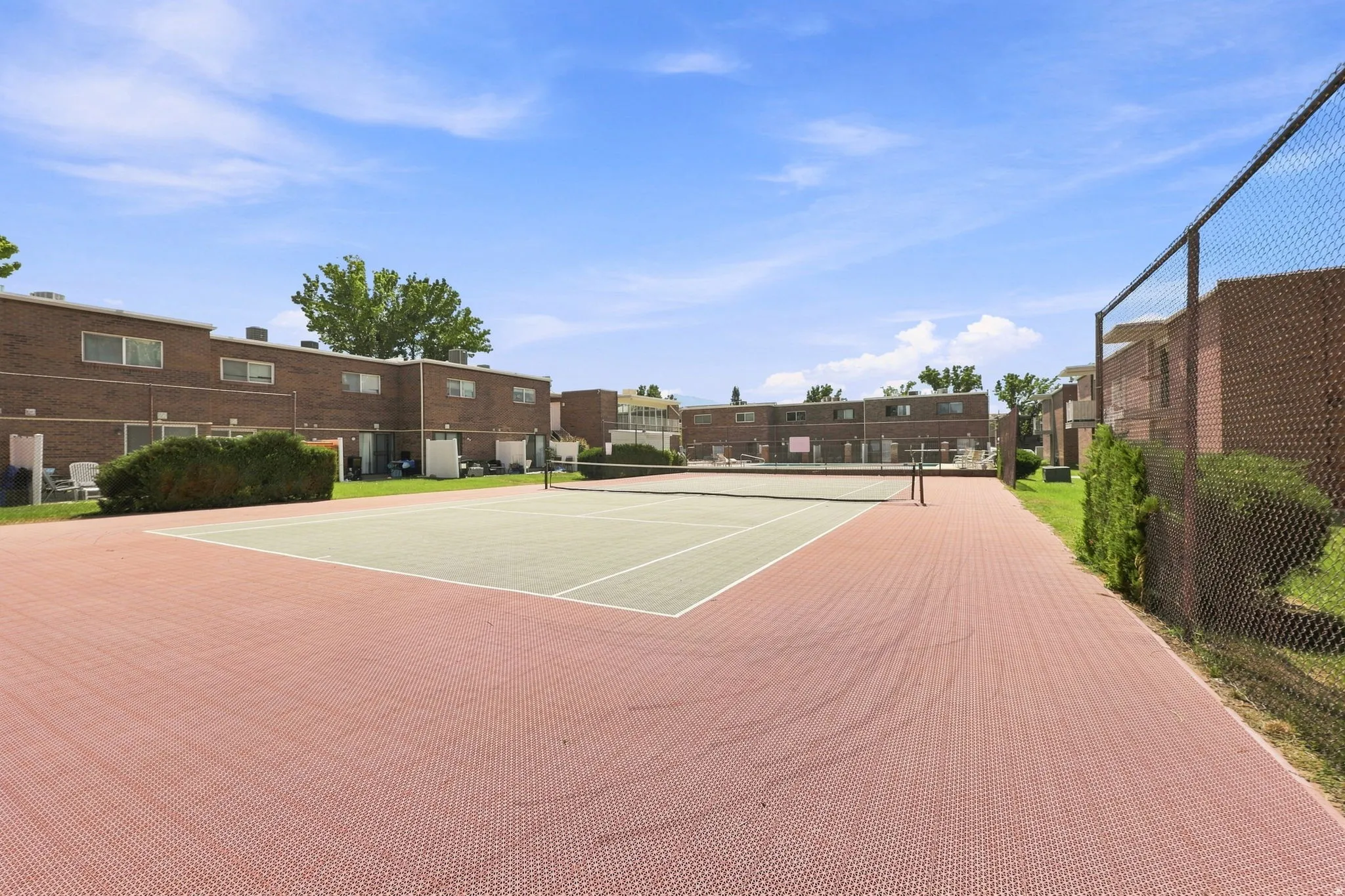 Dedicated recreational court with professional-grade playing surface, bordered by brick hardscaping and perimeter fencing
